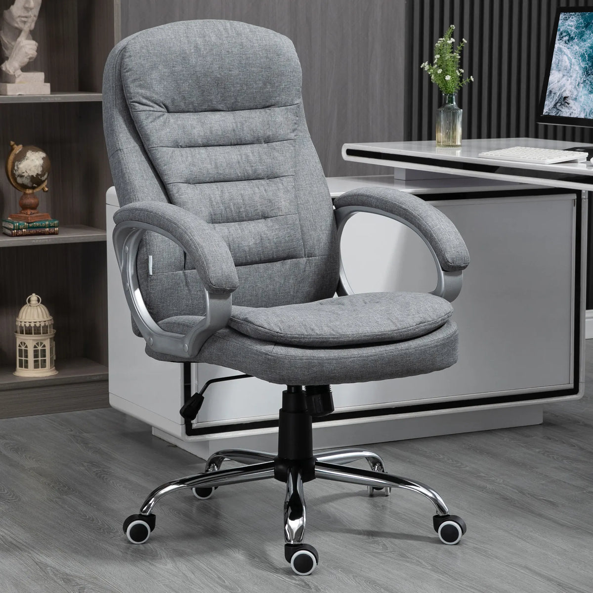 Gray high-back office chair with padded arms and a silver-toned caster base beside a desk.