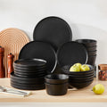 Set of black ceramic plates and bowls on a wooden surface with apples and a white background.