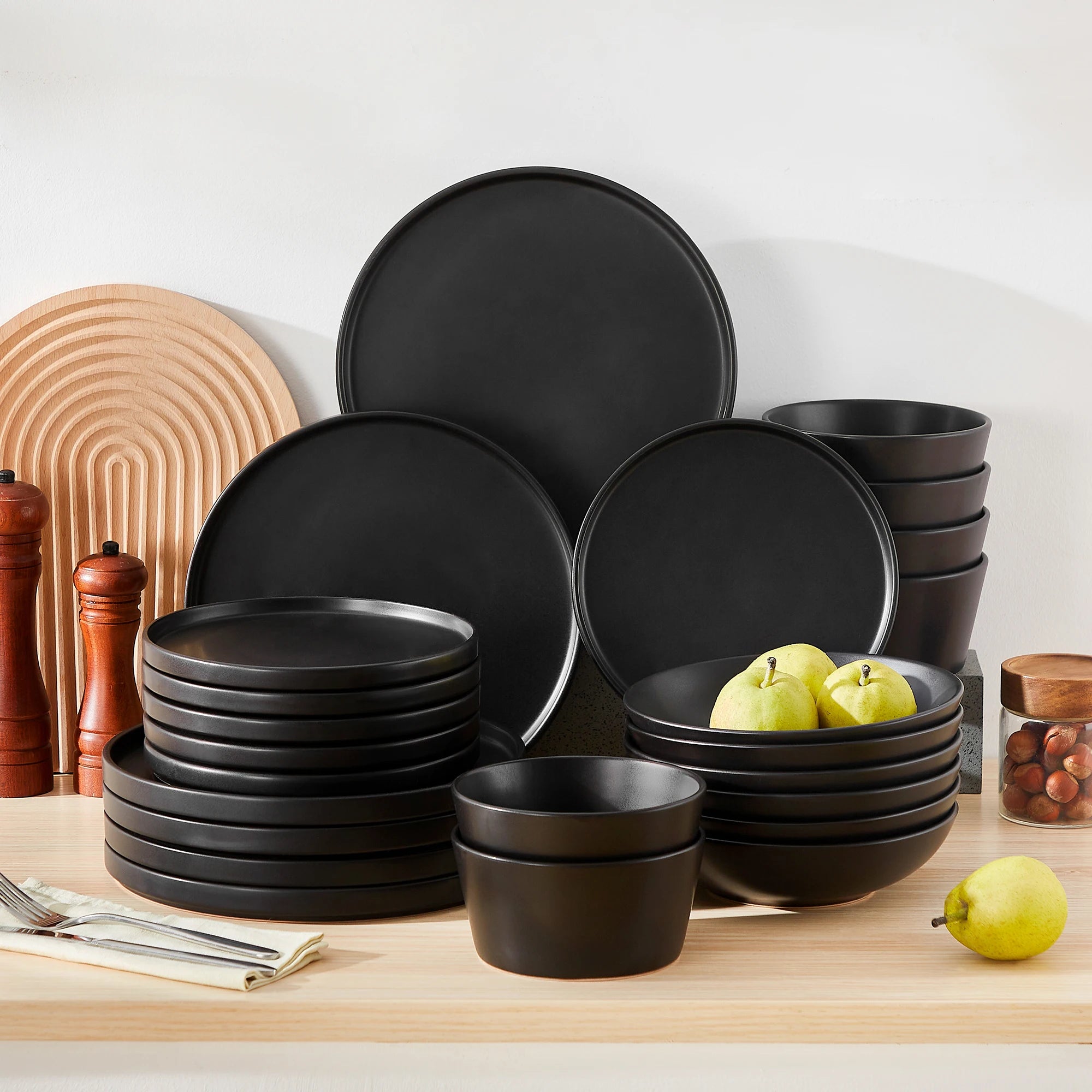 Set of black ceramic plates and bowls on a wooden surface with apples and a white background.