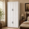 White four-door farmhouse wardrobe with black handles beside a bed
