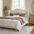 Light-colored upholstered queen bed with a curved wingback headboard in a neutral bedroom.