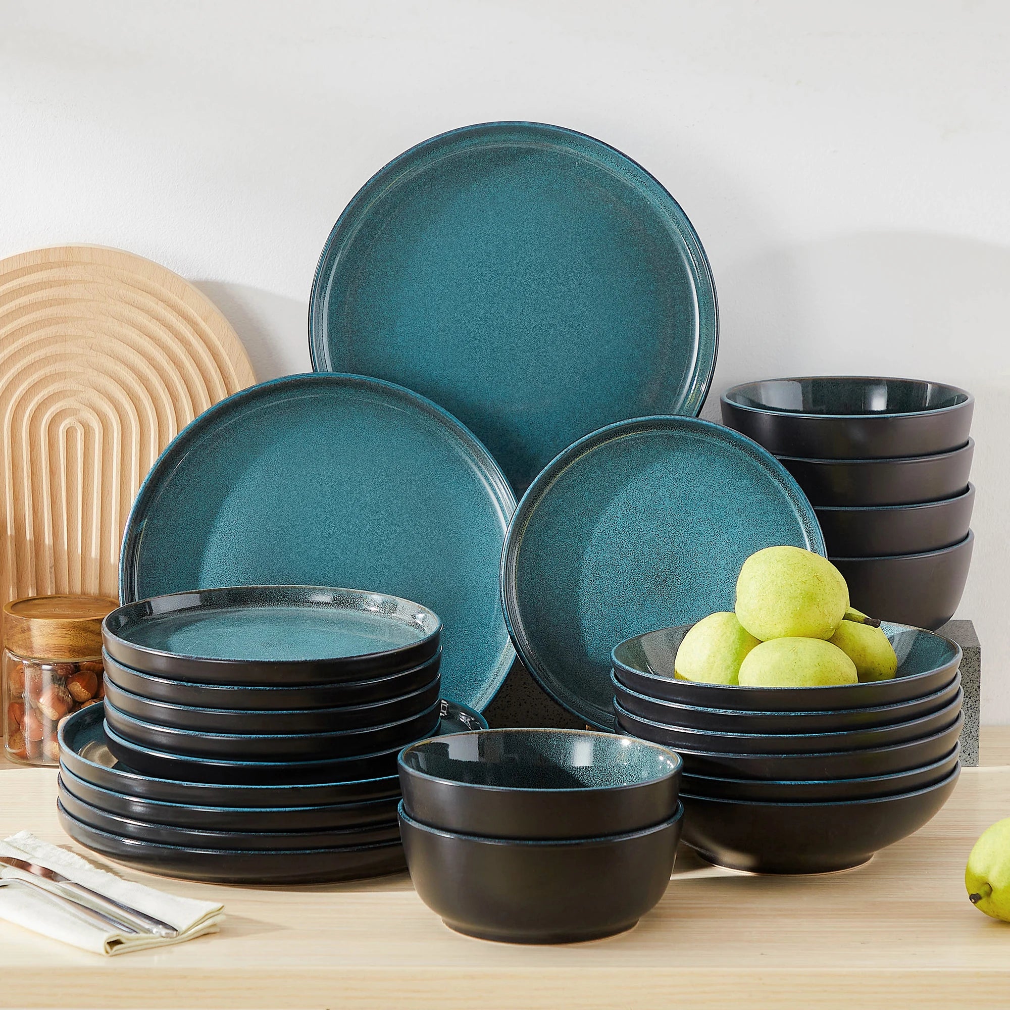 Set of teal and black ceramic dinnerware on a wooden surface with apples.