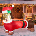 Wagglebright brown dachshund inflatable dressed in a red Santa coat and hat in a Christmas yard.