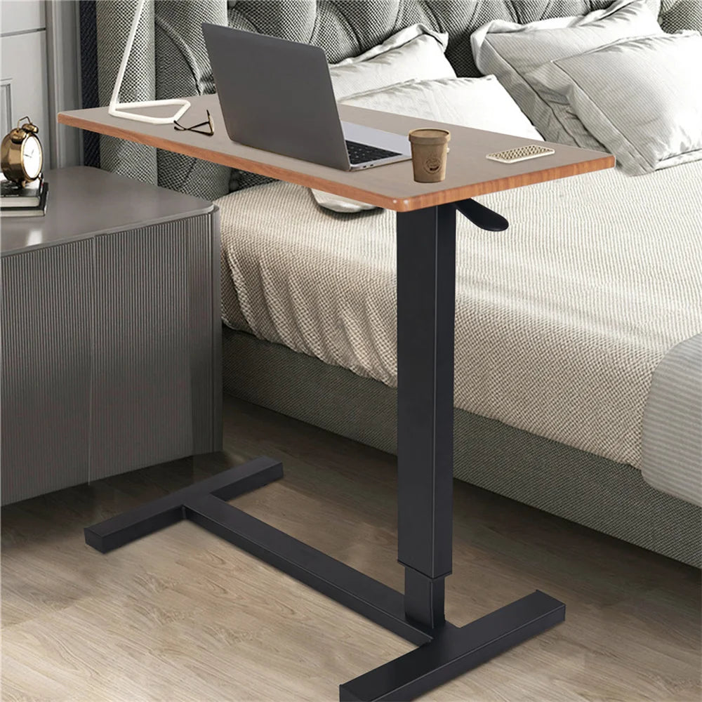 Oak-look overbed table with height-adjustment lever and low black base beside a bed