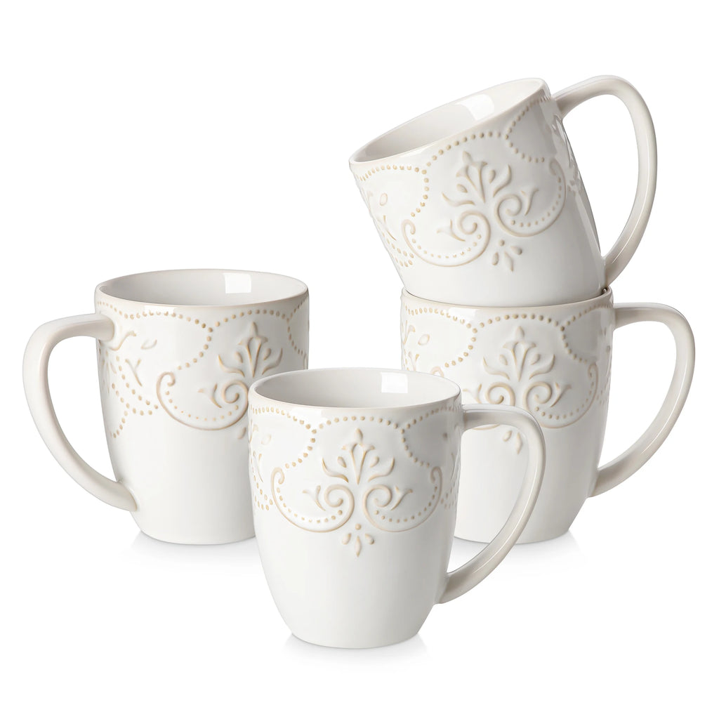 Four white GISELLE mugs with floral scroll relief and tall handles arranged on a white background