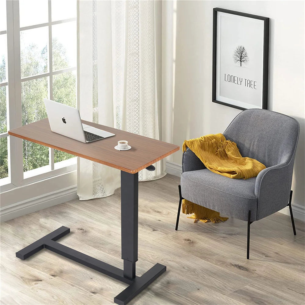 Adjustable oak-look side table holding a laptop beside an upholstered chair