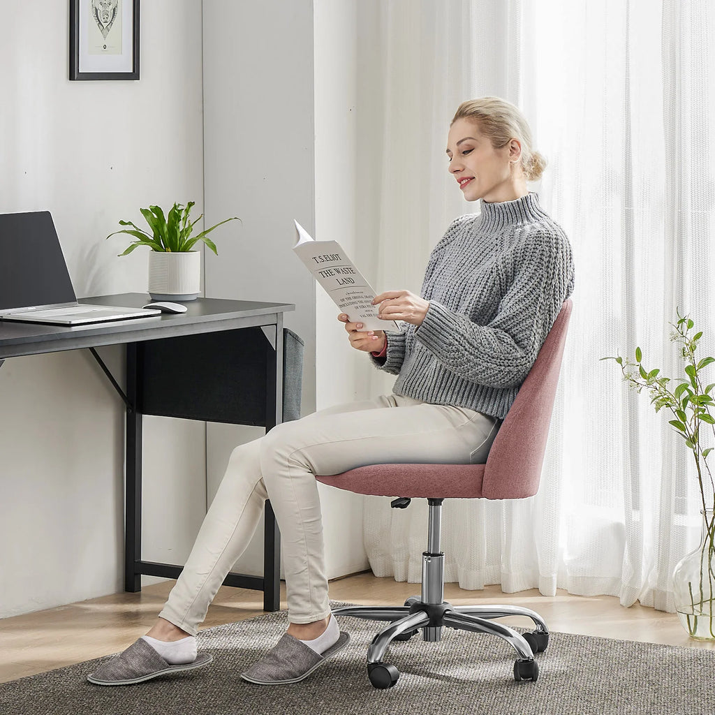 Woman sitting in a pink office chair reading a document in a home office setting.
