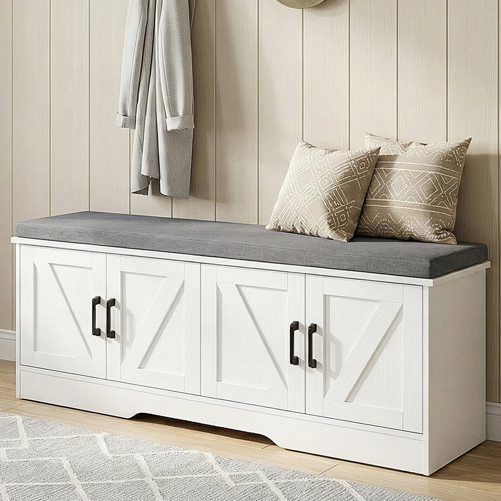 A white storage bench with a gray cushioned seat and two decorative pillows, styled in a hallway with wood-paneled walls and a hanging robe.