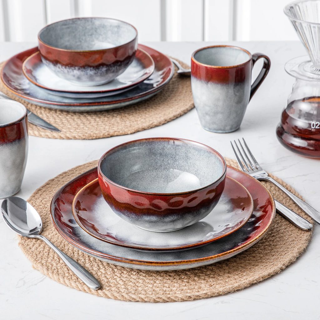 Red and gray plates and bowls layered on woven placemats with matching mugs beside them.